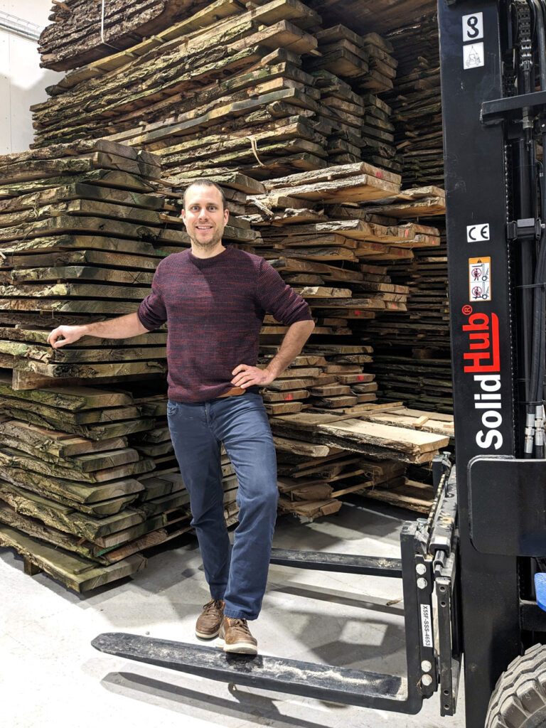 Adrien Meirlaen staat voor een grote stapel hout met naast hem een vorklift.